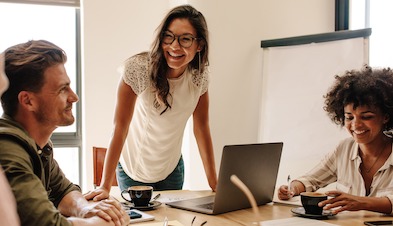 Employees collaborating around laptop with lattes in mugs