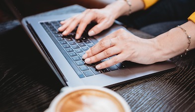 Worker typing on laptop, with cup of coffee